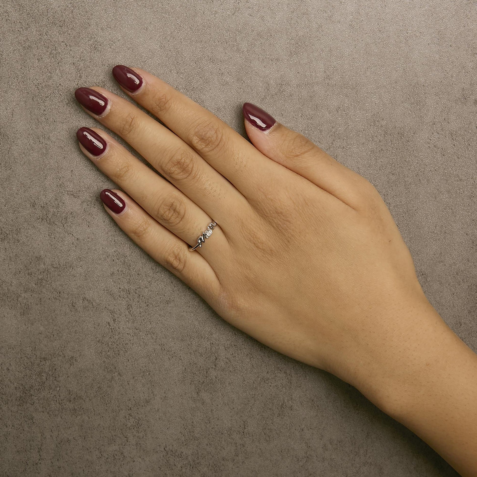 Close-up of a white metal ring with a round white gemstone in prong setting worn on a model's hand, shot from above.