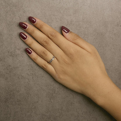Close-up of a white metal ring with a round white gemstone in prong setting worn on a model's hand, shot from above.