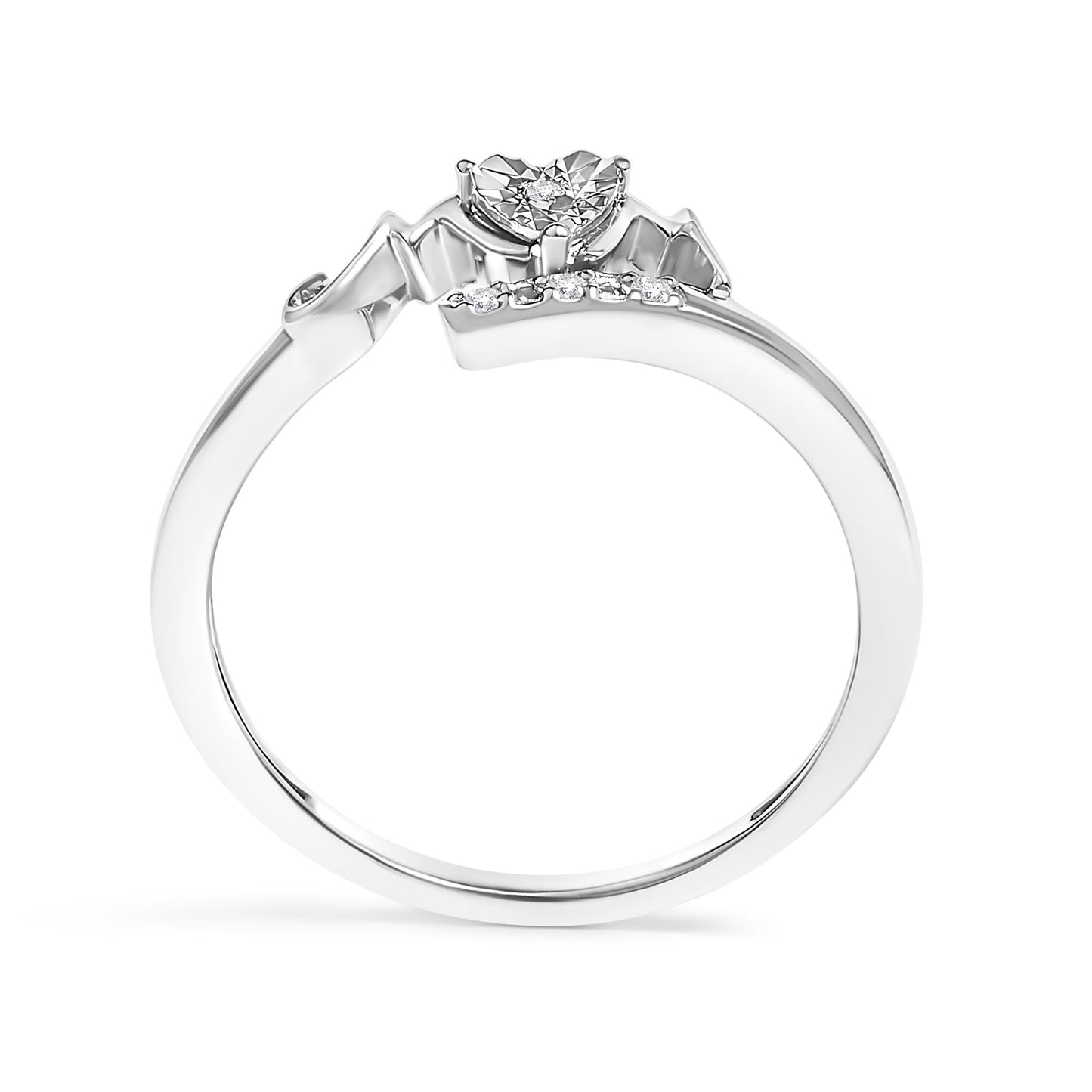Close-up side view of a white metal ring with a heart-shaped setting featuring a round white gemstone in prong setting, accompanied by a row of smaller round white gemstones along the band.