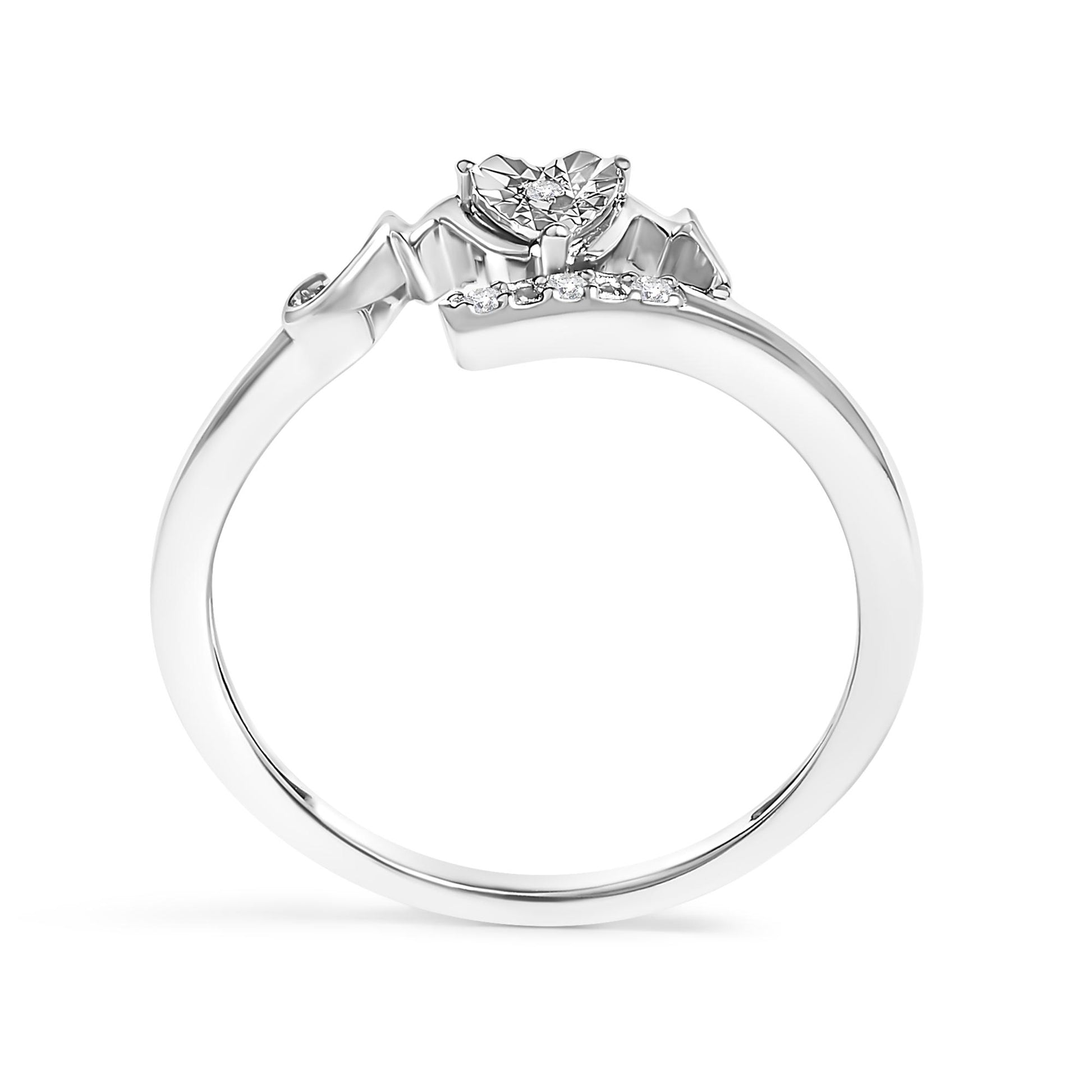 Close-up side view of a white metal ring with a heart-shaped setting featuring a round white gemstone in prong setting, accompanied by a row of smaller round white gemstones along the band.