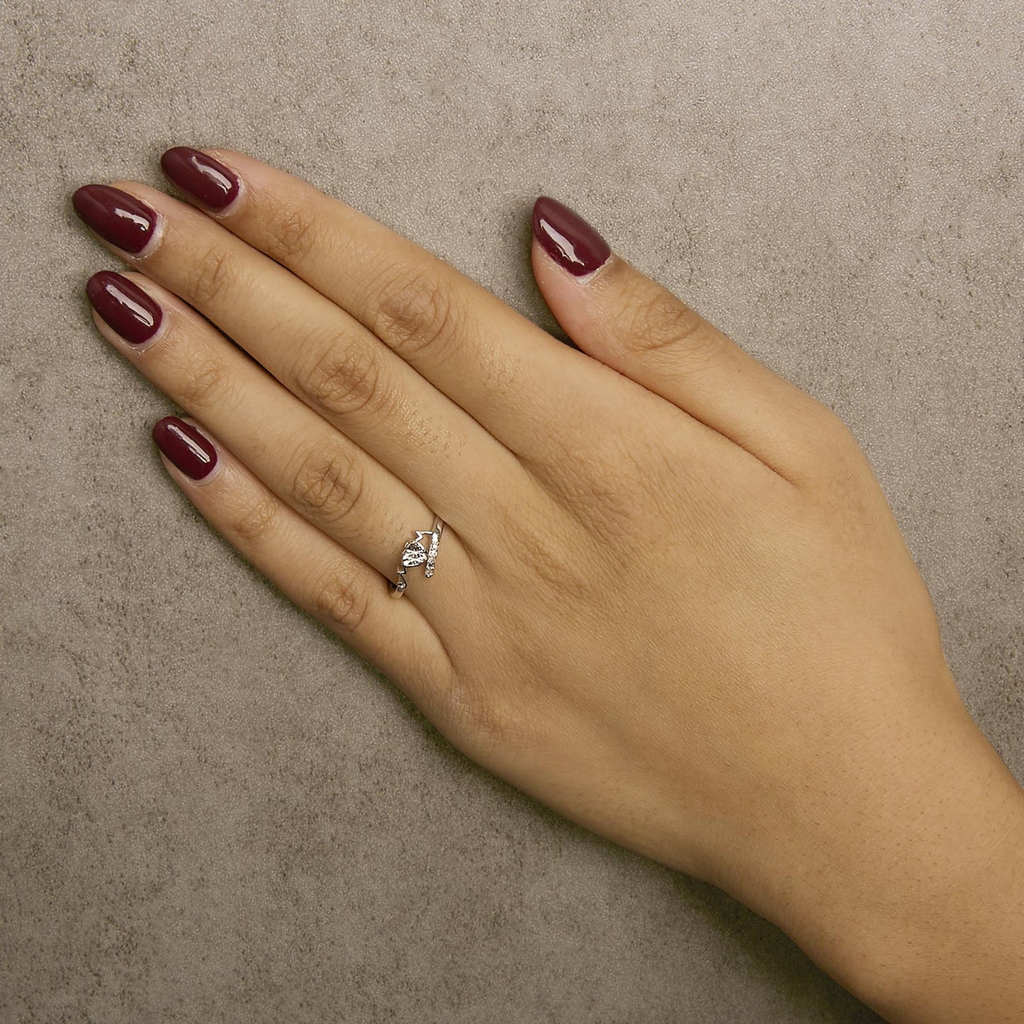 White metal ring with four round white gemstones in prong settings, worn on a model's hand, top-down angle.