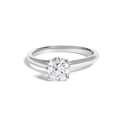 Front angle close-up of a white metal ring featuring a single round white gemstone in a four-prong setting, shown on a white background.