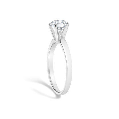 Close-up view of a white metal ring with a single round white gemstone in a four-prong setting, shown upright on a white background.