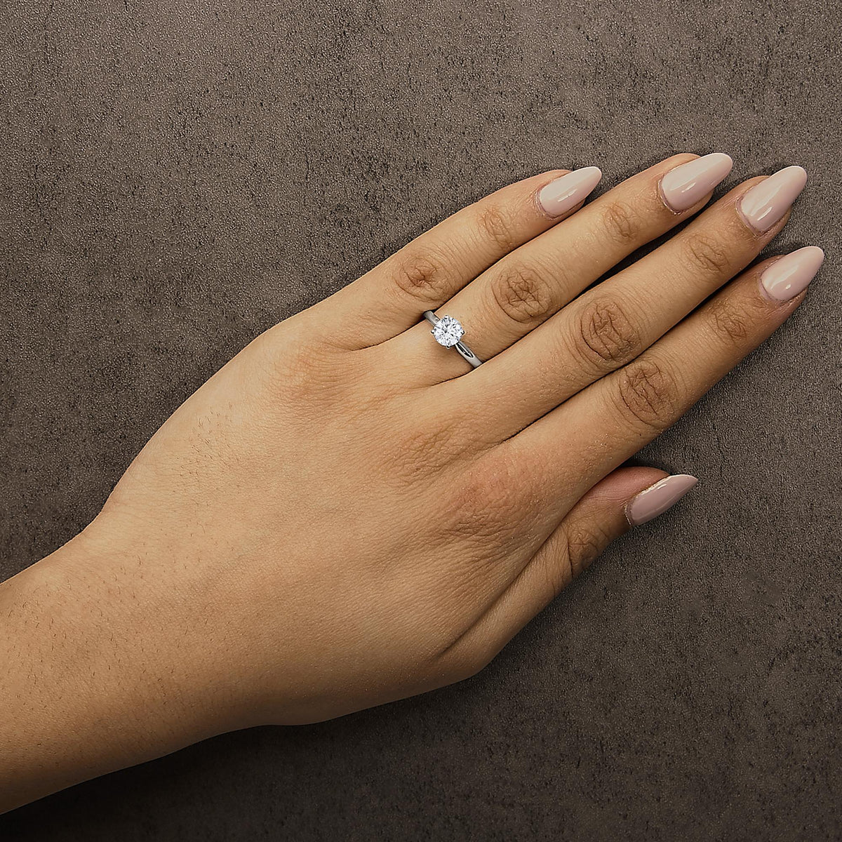 White metal ring with a single round white gemstone in a four-prong setting, shown worn on a model's hand from a top angle.