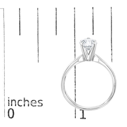 Close-up front angle of a white metal ring with a single round white gemstone in a four-prong setting placed on a measurement scale.