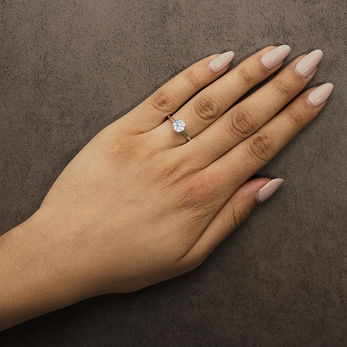 Yellow ring with a round white gemstone in a 4-prong setting, shown worn on a model’s hand from a top angle.