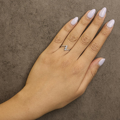 White metal ring with three white round gemstones in a shared prong setting, shown worn on a model's hand from a top-down angle.