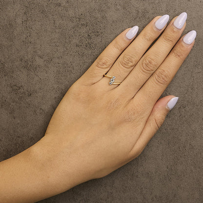 Yellow metal ring with three white round gemstones in a shared prong setting, shown worn on a model's finger from a top angle.
