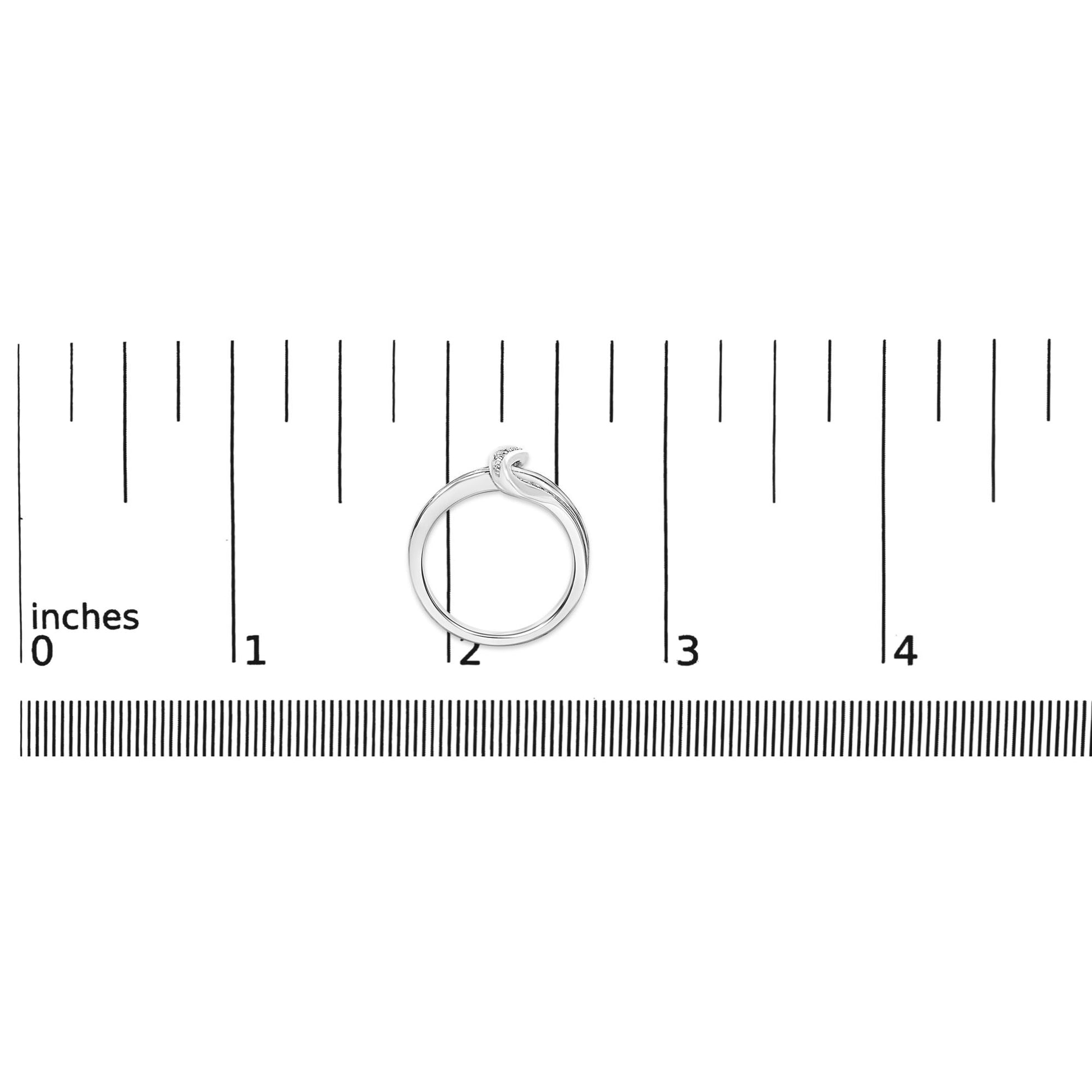 White metal ring with an abstract knot design accented with round blue and white gemstones in prong settings, shown on a ruler scale from a top-down view.