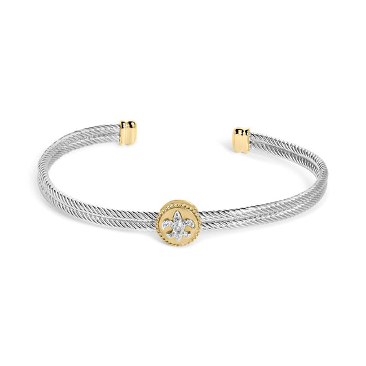 Open bracelet with twisted white metal bands, yellow metal accents on ends and center featuring a round yellow metal medallion adorned with a fleur-de-lis pattern set with white round gemstones, shown at a slight angle.