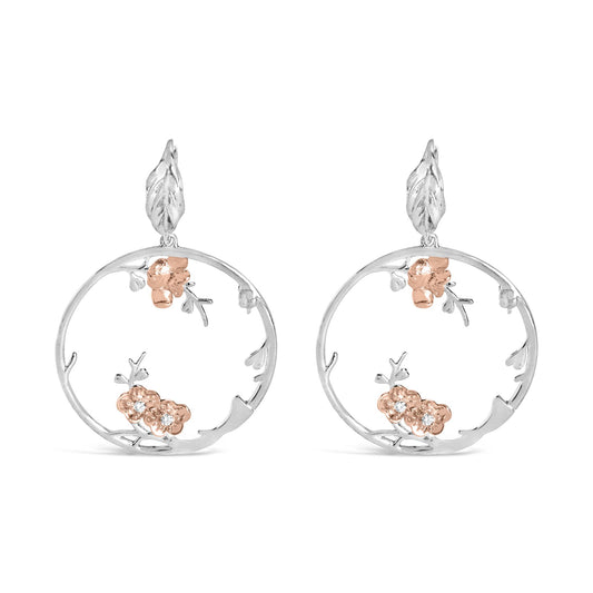 Front view of round hoop earrings with white and rose metal colors, featuring delicate floral designs with small white gemstones in a 4-prong setting.