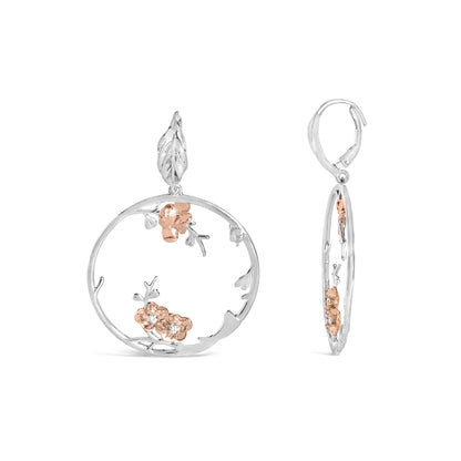 Front and side view of circular earrings with white and rose metal floral design and white round gemstones set in rose metal flowers.