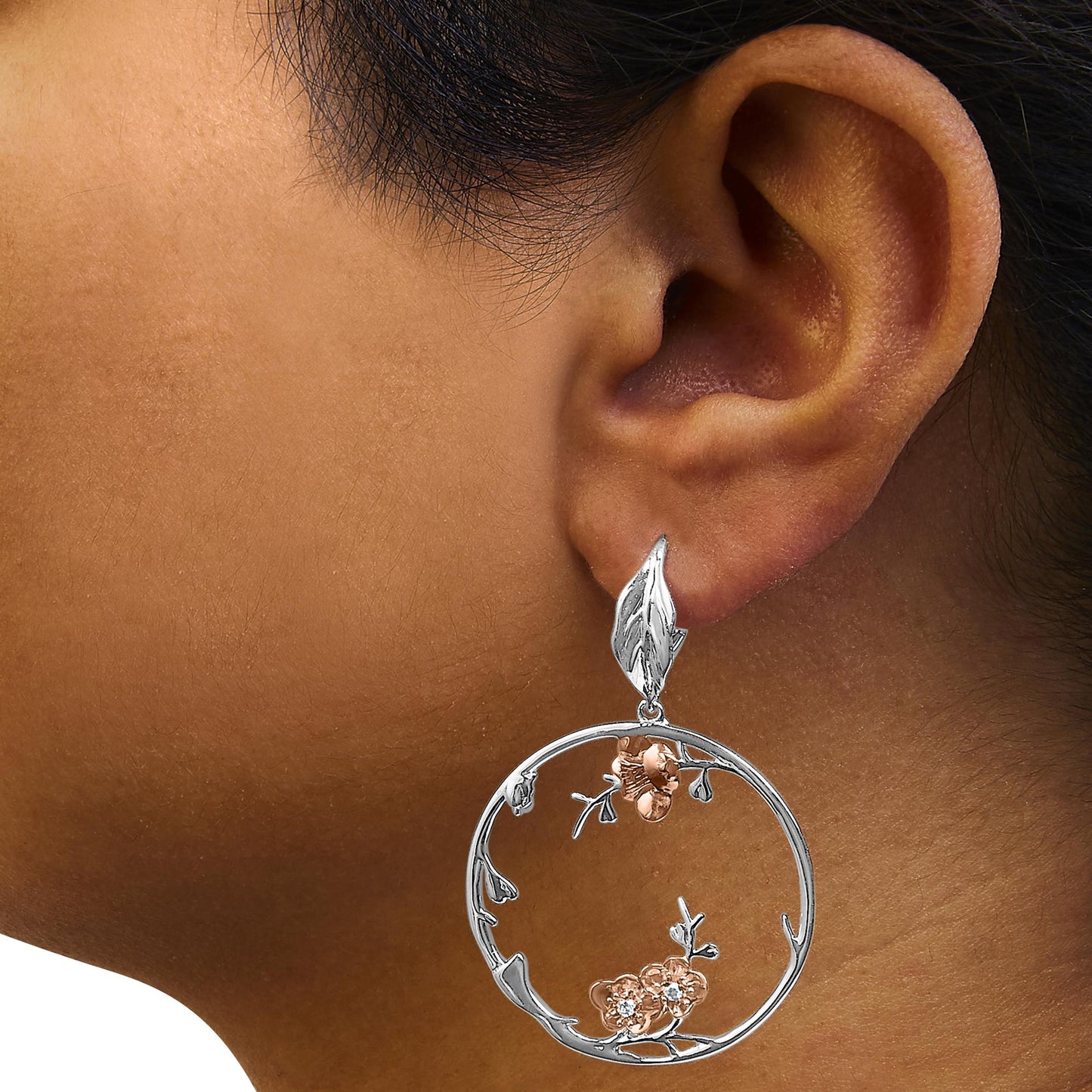 Close-up side view of a white and rose metal hoop earring on a model's ear, featuring floral accents with white gemstones.