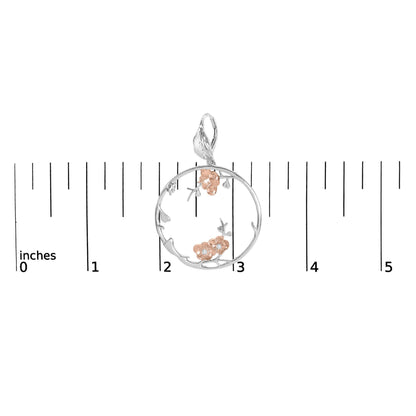 Top-down view of a circular earring with white and rose metal colors, featuring floral accents with white gemstones, placed on a ruler for size reference.