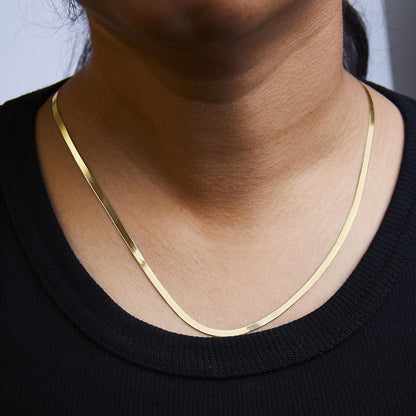 Close-up front view of a yellow flat chain necklace shown worn on a model's neck.