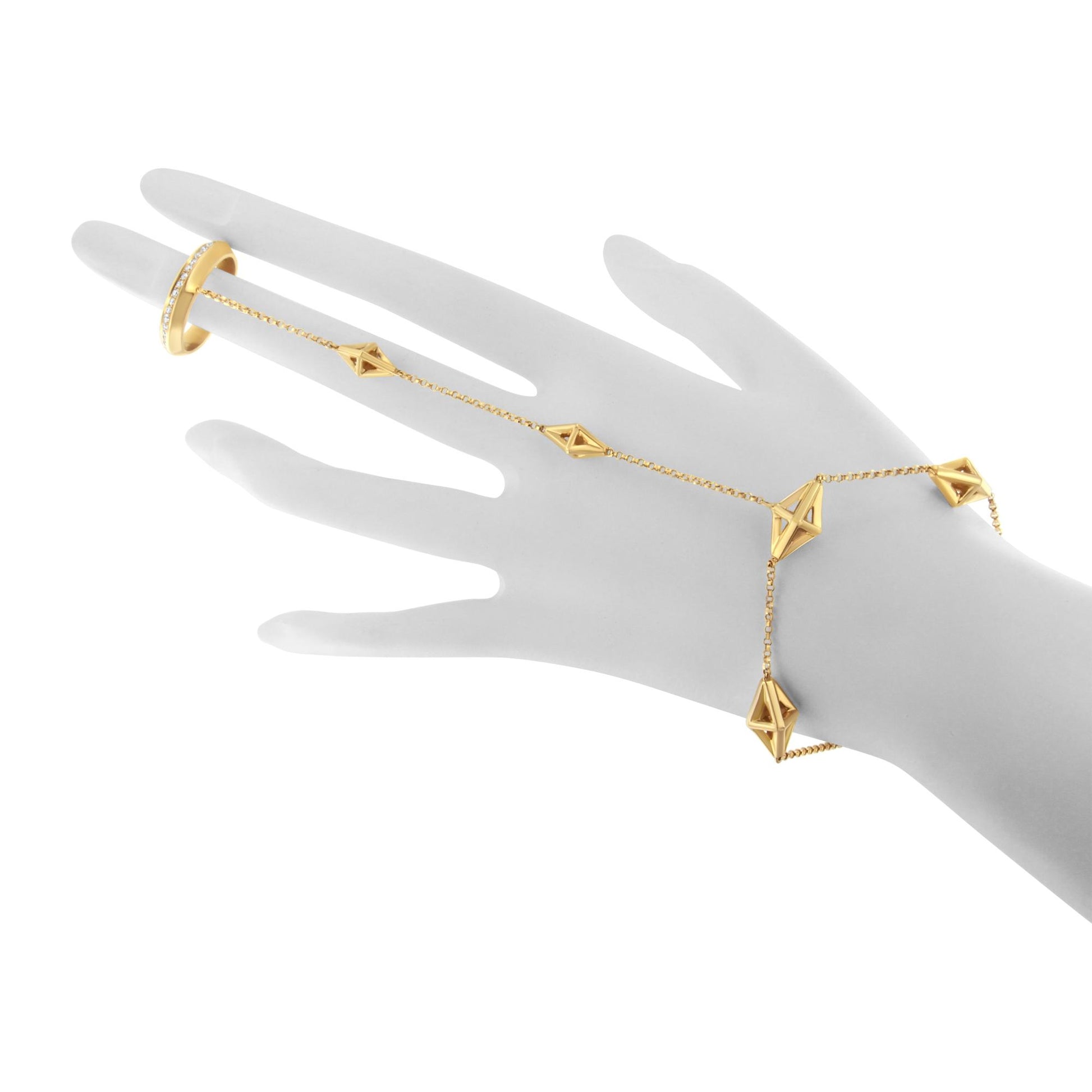 Yellow metal bracelet with geometric shapes and a matching ring with white gemstones in pave setting, displayed on a gray hand model, shown from a top angle.