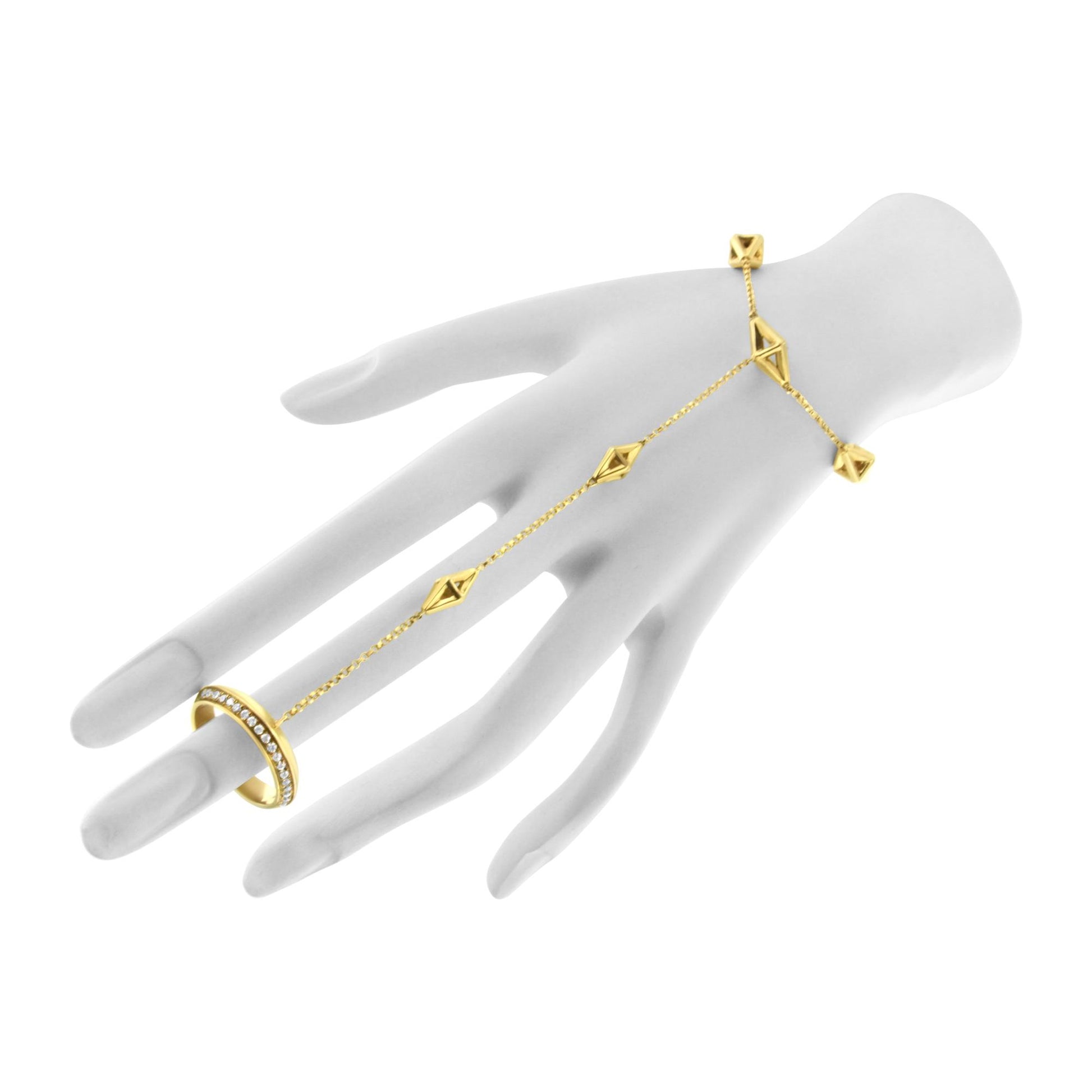 Yellow metal bracelet with geometric shapes and a row of white gemstones in pave setting, shown worn on a hand model, angled from above.
