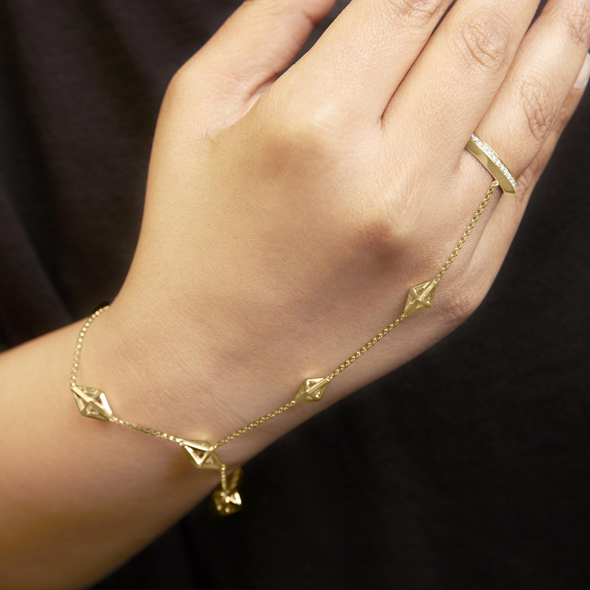 Close-up shot of a yellow bracelet with geometric elements and a matching ring adorned with round white gemstones in a pave setting, worn on a model's hand.