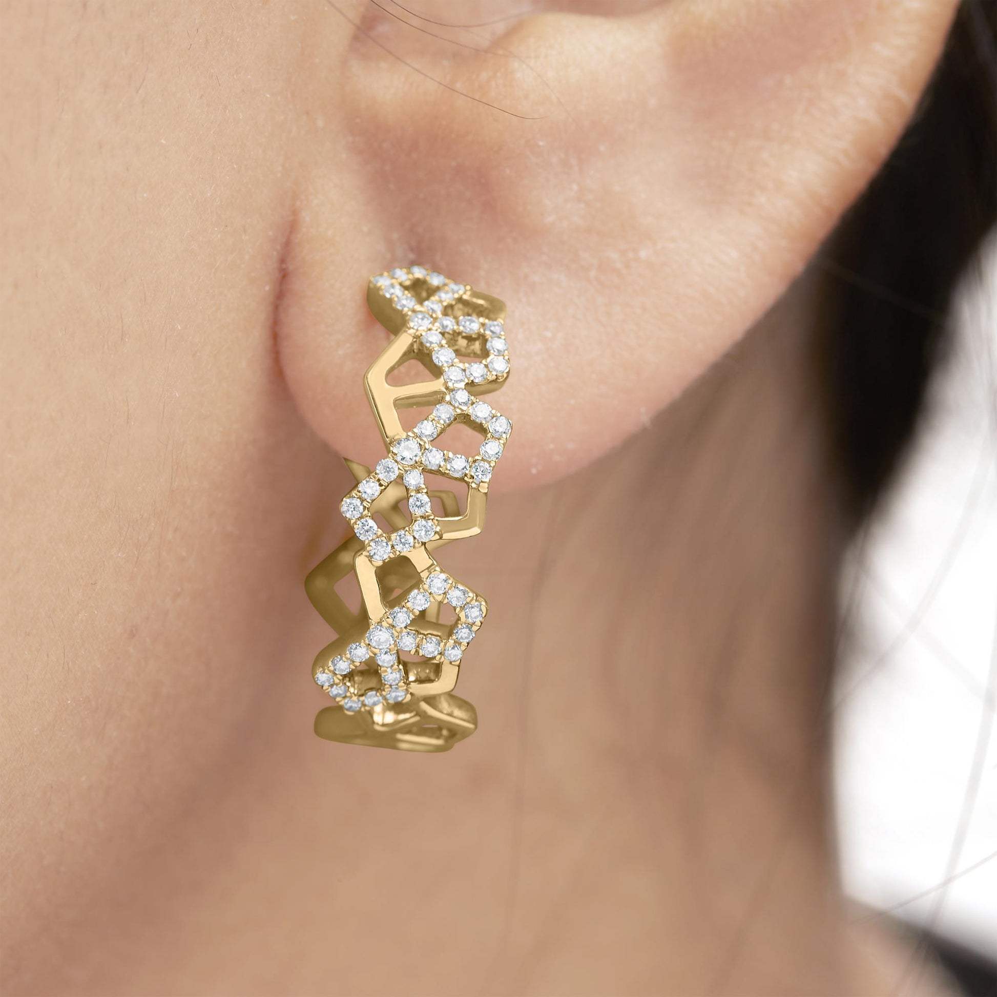 Close-up side view of a yellow metal earring on a model's ear, featuring multiple open geometric shapes partially outlined with small white gemstones in a pave setting.