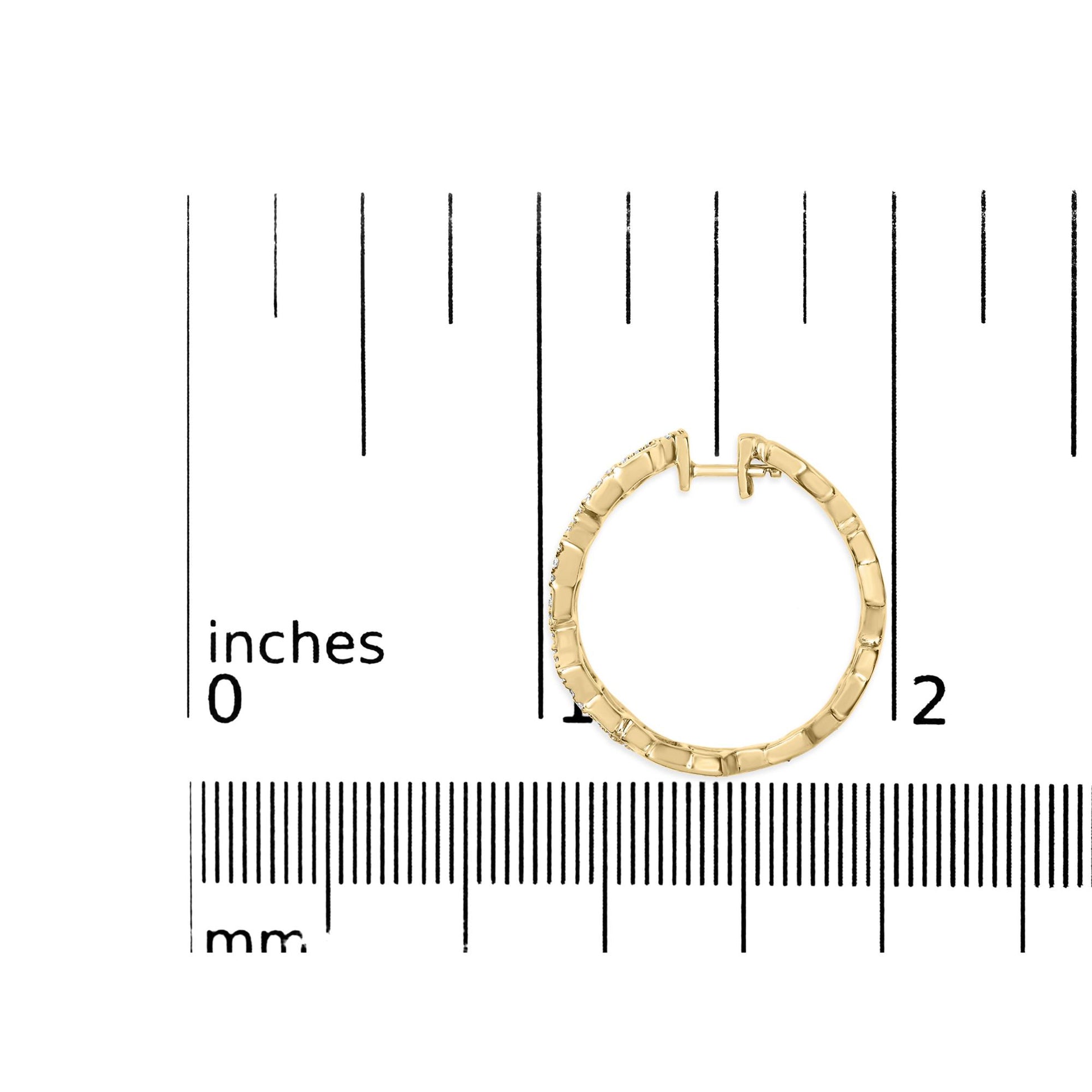 Close-up top view of a yellow metal hoop earring with round white gemstones in pave setting, placed on a ruler for size reference.