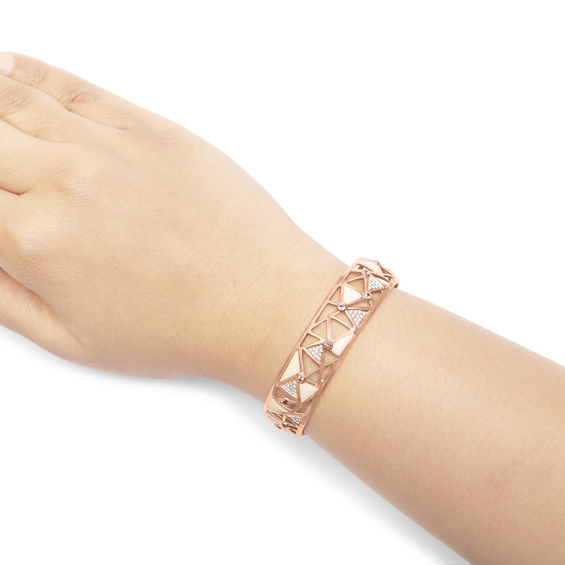 Rose-colored bracelet with geometric cutout design, featuring white gemstones in pave setting and pink round gemstones in bezel setting, shown on a model's wrist from a top-side angle.