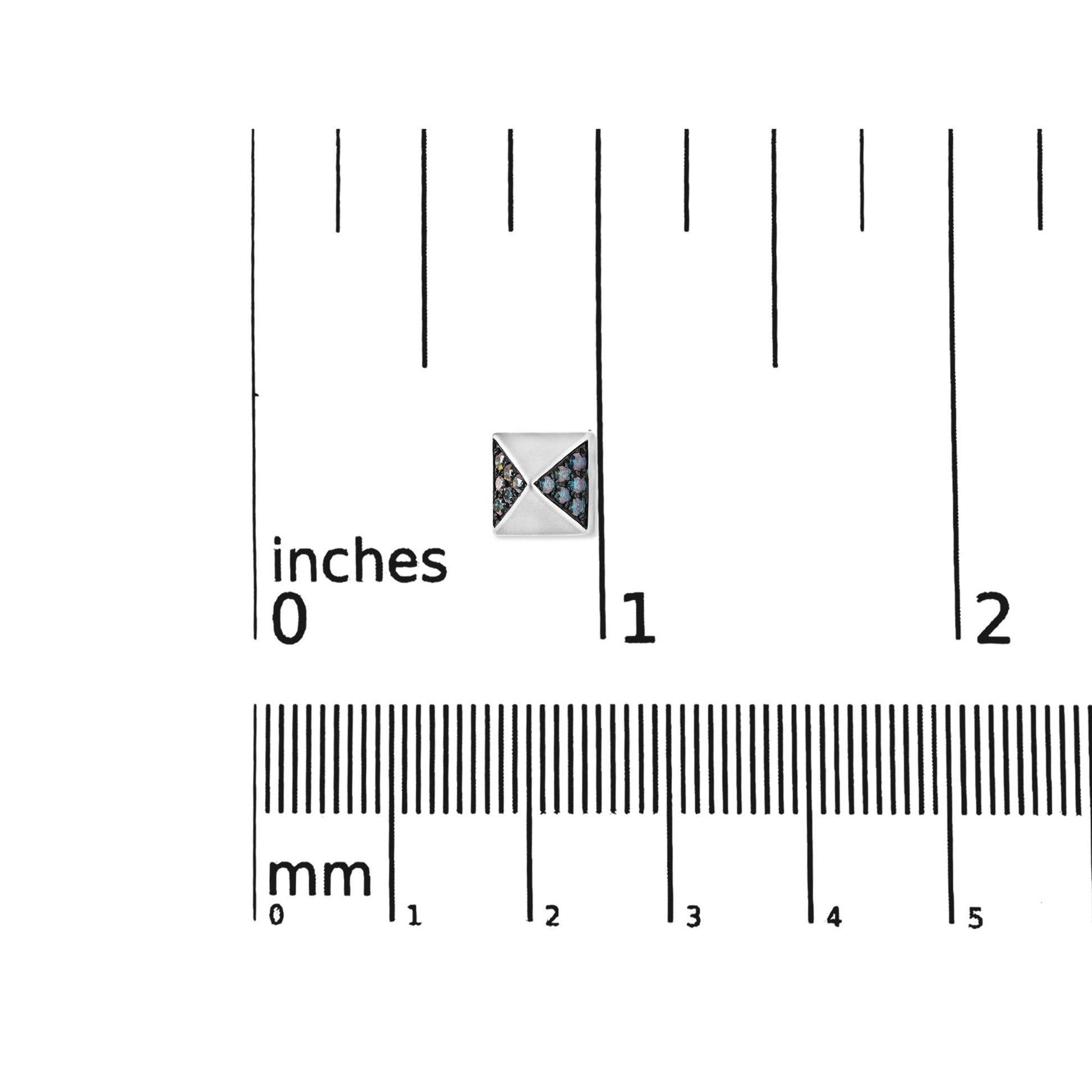 Close-up, top-down view of a small white metal earring with triangular sections inlaid with round blue gemstones, placed on a ruler for size reference.