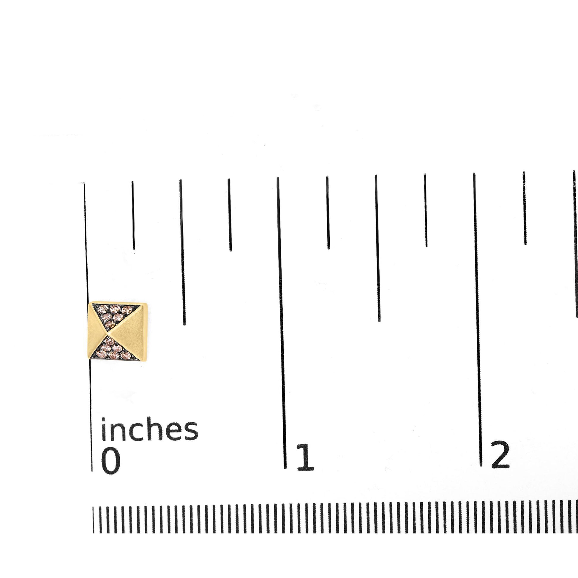 Close-up front angle of a small rose metal pyramid-shaped earring with round brown gemstones in prong setting, placed on a ruler for size reference.