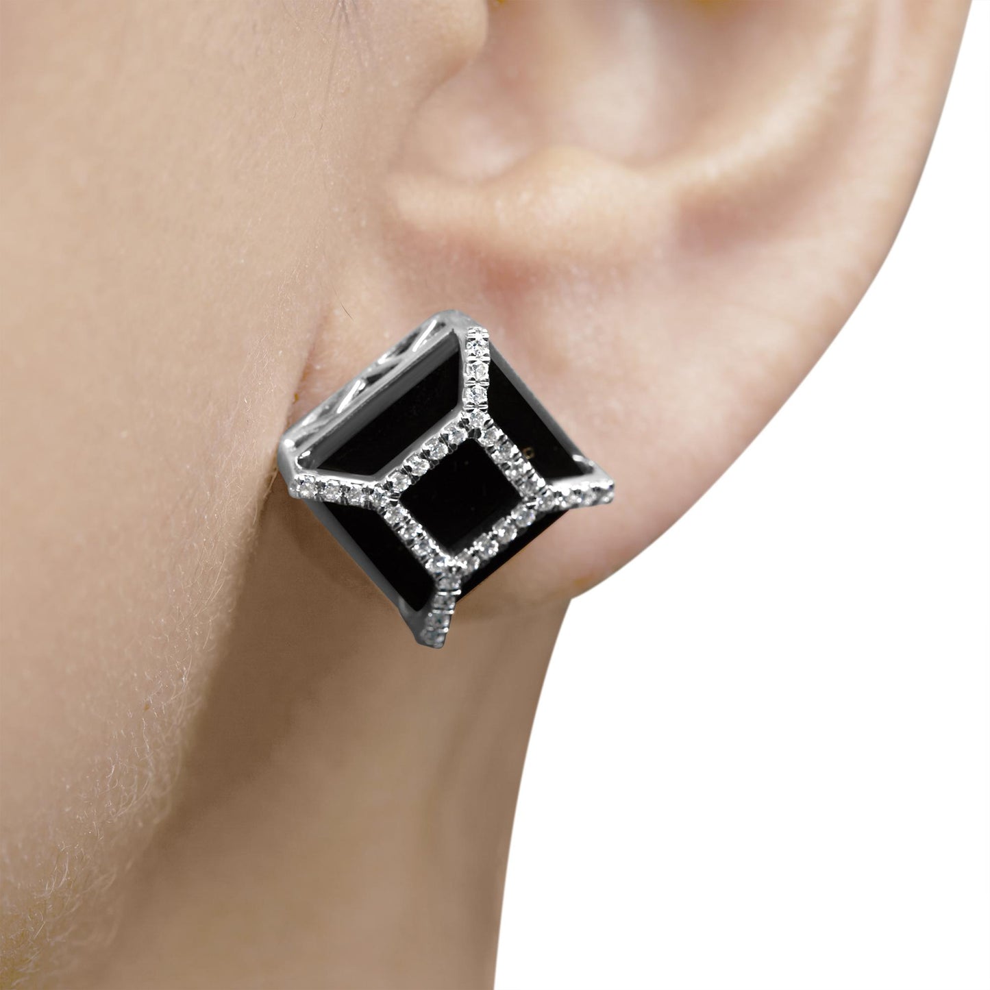Close-up side view of a white metal earring on a model's ear, featuring black cushion-shaped gemstones surrounded by round white gemstones in pave setting.