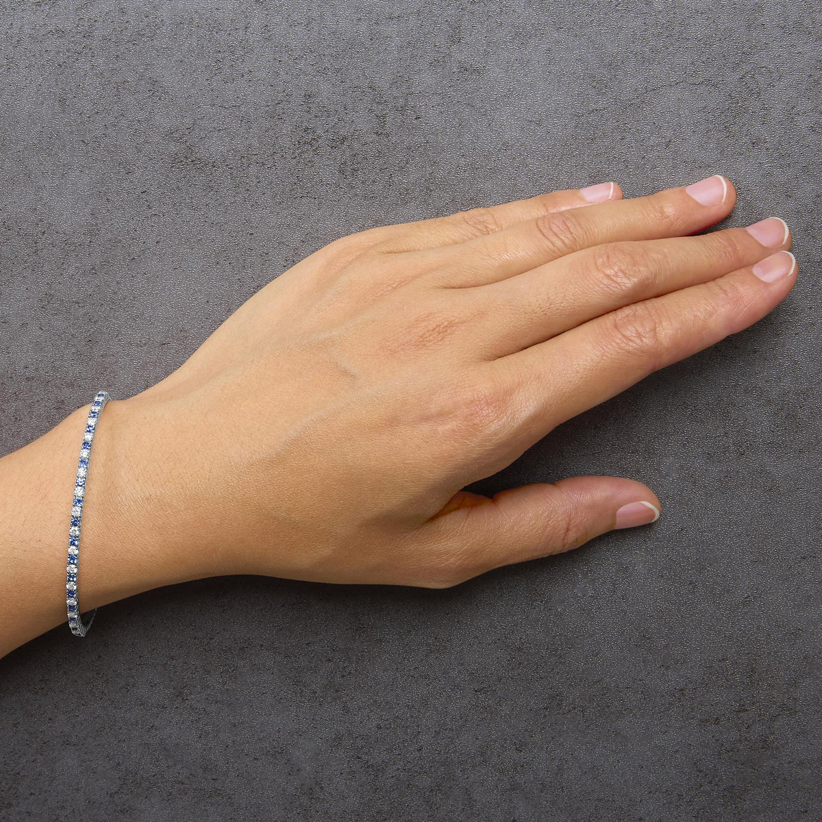 Close-up side angle of a model's hand showing a white bracelet adorned with alternating round blue and white gemstones in prong settings.