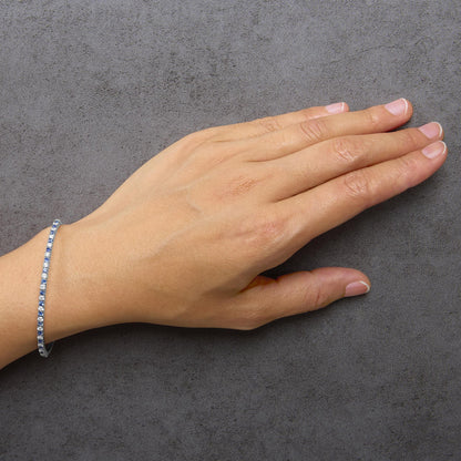 Close-up side angle of a model's hand showing a white bracelet adorned with alternating round blue and white gemstones in prong settings.