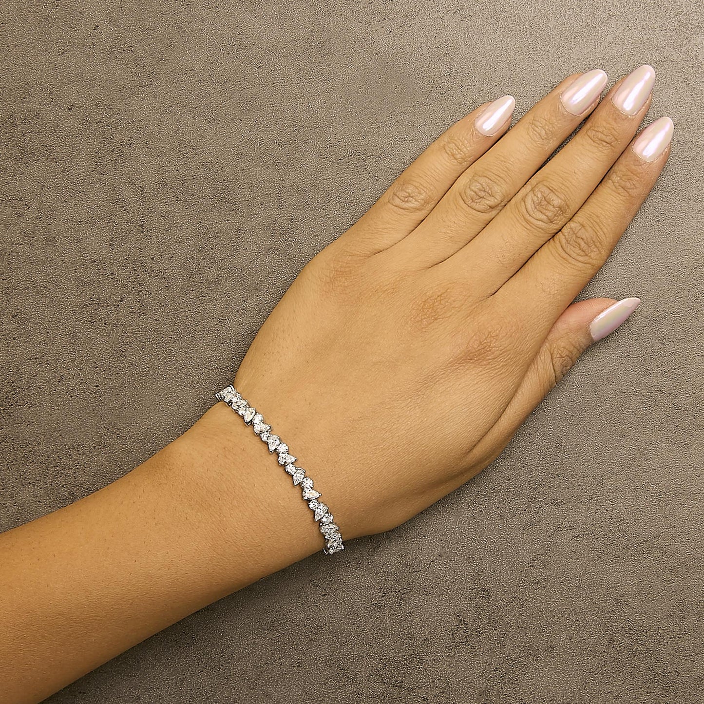 White metal bracelet with alternating pear-shaped and round white gemstones in 3-prong settings, shown on a model's wrist, top-down angle.