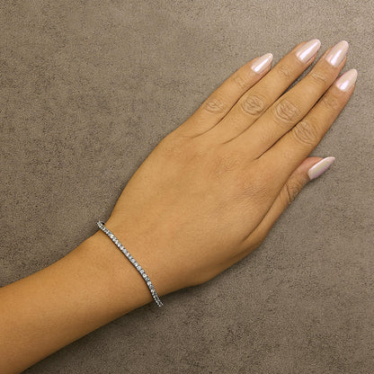 White metal bracelet with alternating white and blue round gemstones in 4-prong settings, shown on a model's wrist from a top-down angle.