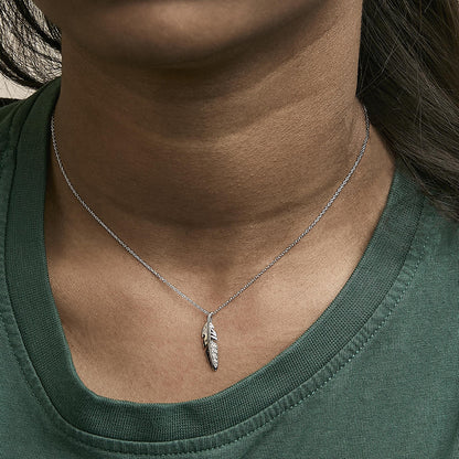 Close-up front view of a model wearing a white metal necklace with a feather-shaped pendant featuring a pave setting of white round gemstones.