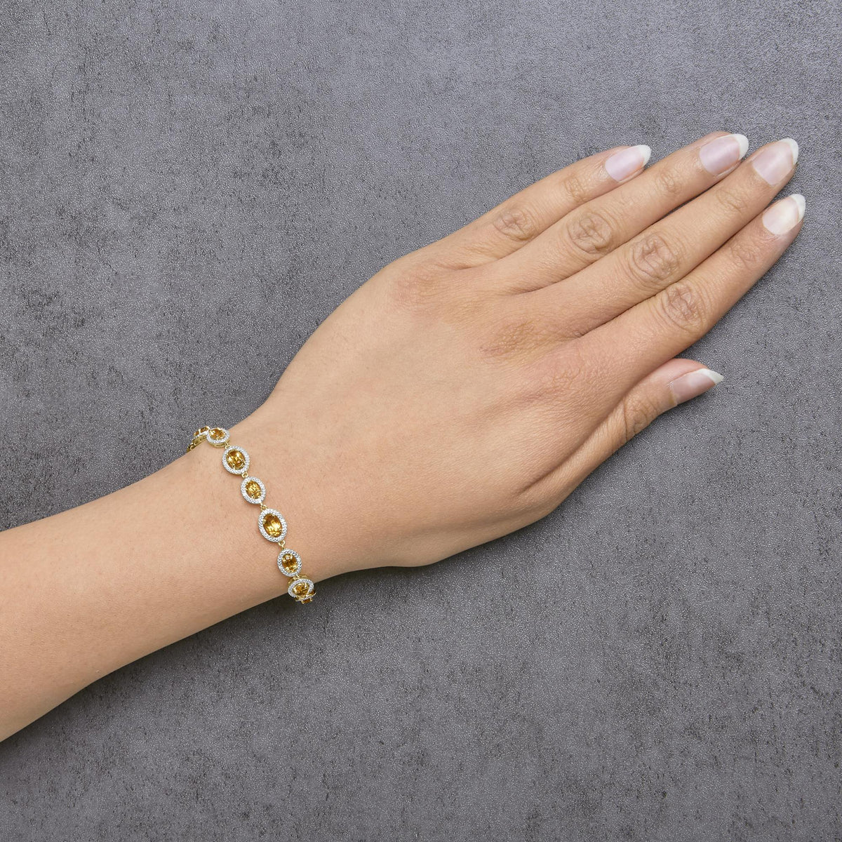 Yellow bracelet with oval yellow gemstones surrounded by small white gemstones in a round setting, shown worn on a model's wrist from a top angle.