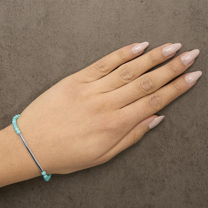 White metal bracelet with small turquoise beads on the sides and a smooth horizontal bar centerpiece, shown worn on a model's wrist, top-down angle.