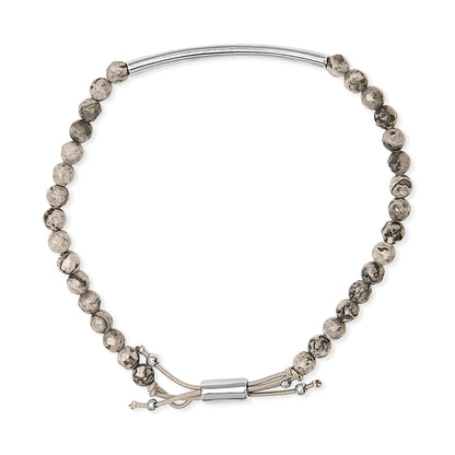 Top-down view of a white metal bracelet featuring patterned round beads and an adjustable cord with metal ends.