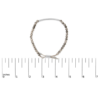 White metal bracelet with round speckled beads and adjustable closure shown on a flat measuring scale, top-down angle.