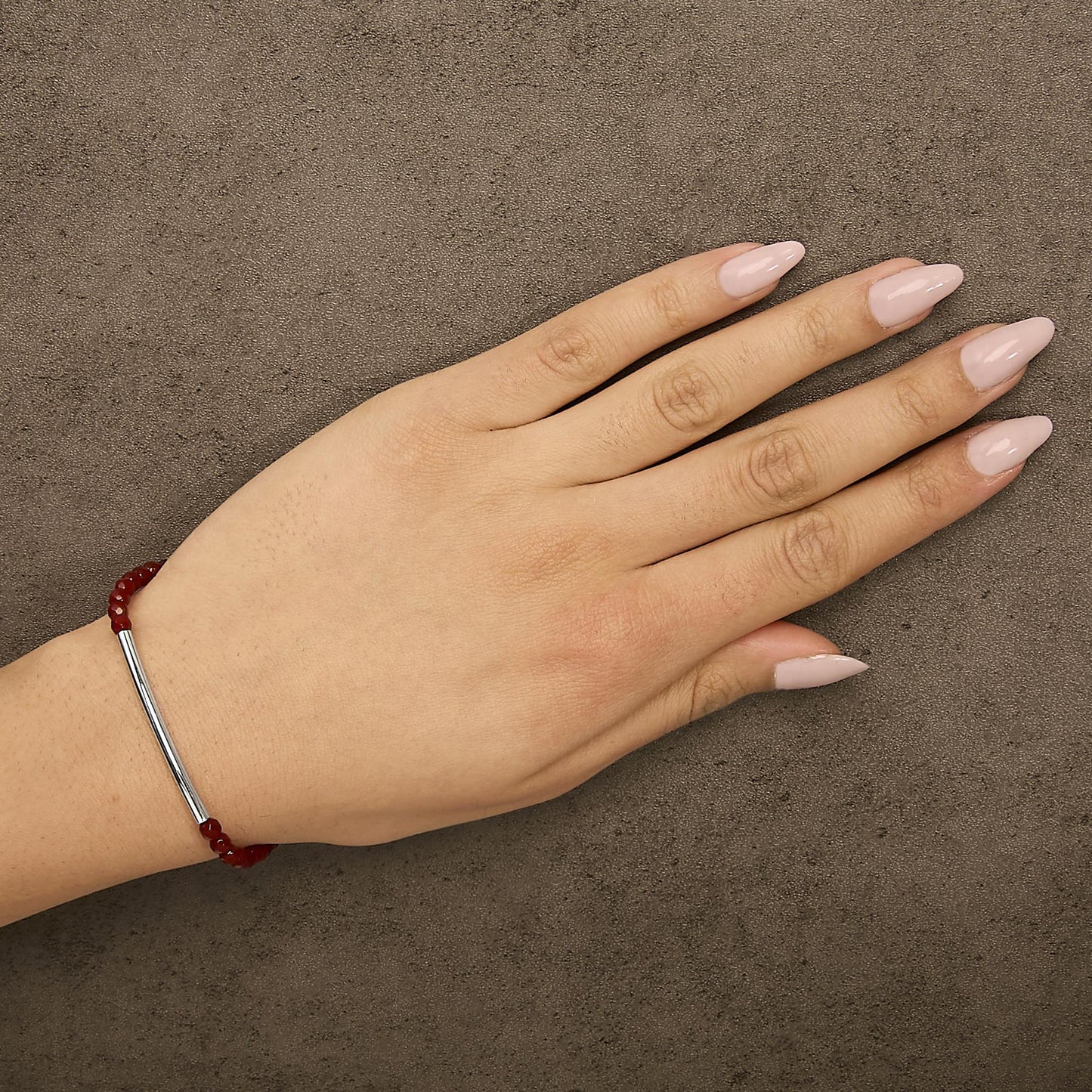 Bracelet with white metal bar and red gemstone beads shown worn on a model’s left wrist, top view angle.