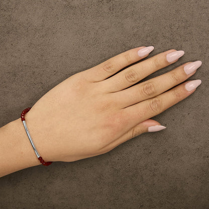 Bracelet with white metal bar and red gemstone beads shown worn on a model’s left wrist, top view angle.