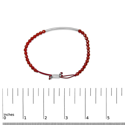 White metal bracelet with red gemstones and a red cord, shown on a scale, front angle.
