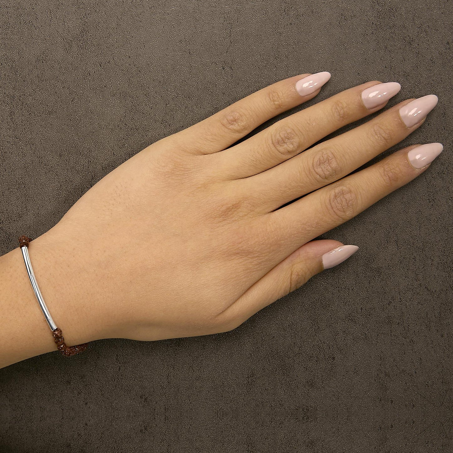 Bracelet with a curved white metal bar and brown gemstone beads, shown worn on a model's wrist, top-down angle.