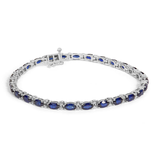 Angled view of sterling silver tennis bracelet showcasing alternating oval blue sapphires and diamond accents on white background
