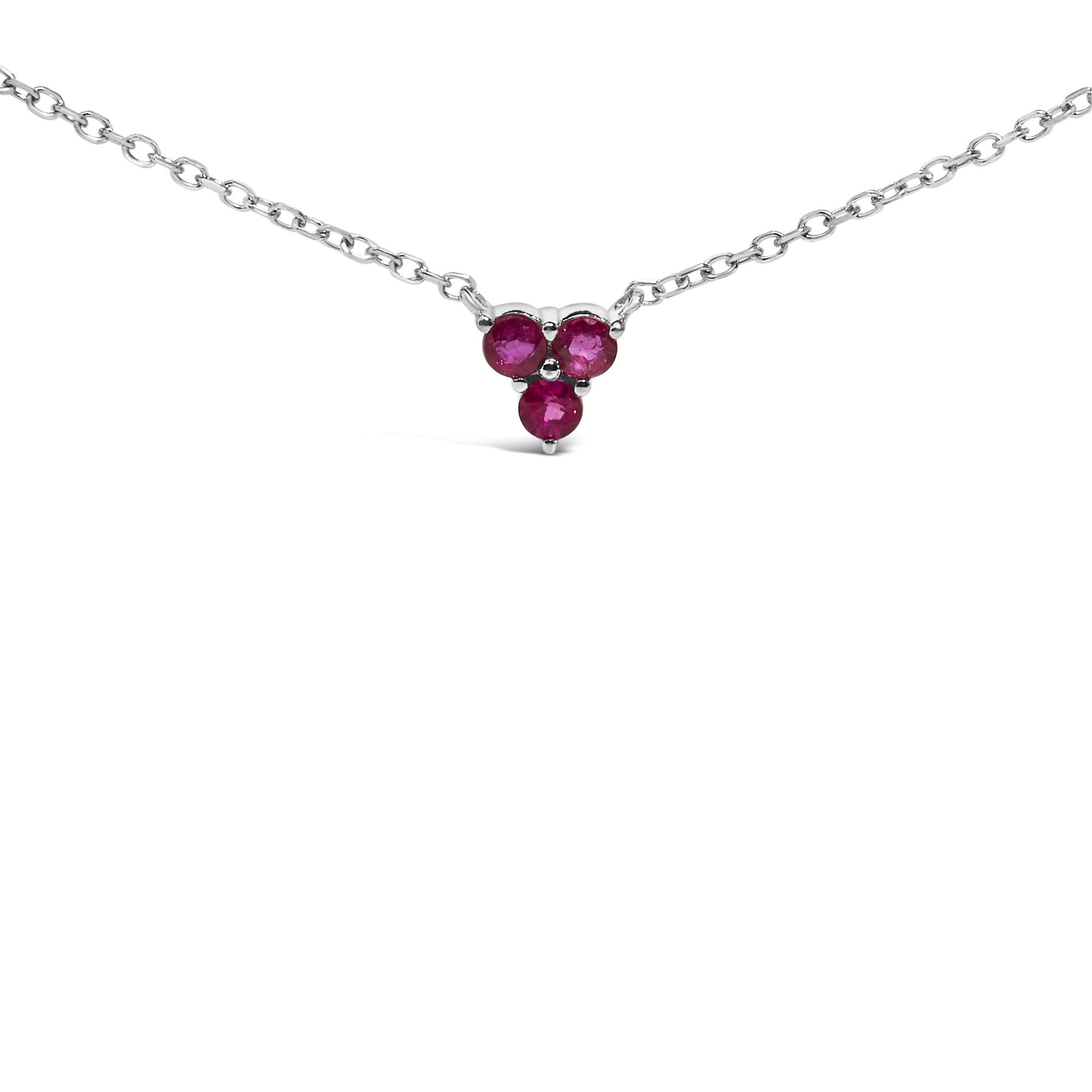 Close-up front view of a white necklace with a pendant featuring three round red gemstones arranged in a triangular cluster, shown on a white background.