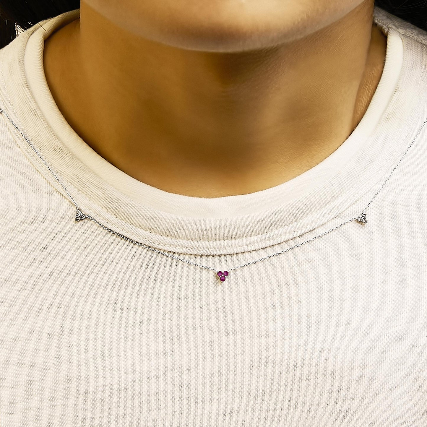 White metal necklace with a small pendant featuring round red and white gemstones in prong settings, shown worn on a model from the front angle.