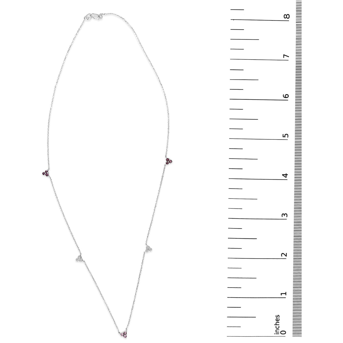 White metal necklace shown on a scale, featuring small triangular clusters of red and white round gemstones in prong settings spaced along a delicate chain. The image is a top-down view.