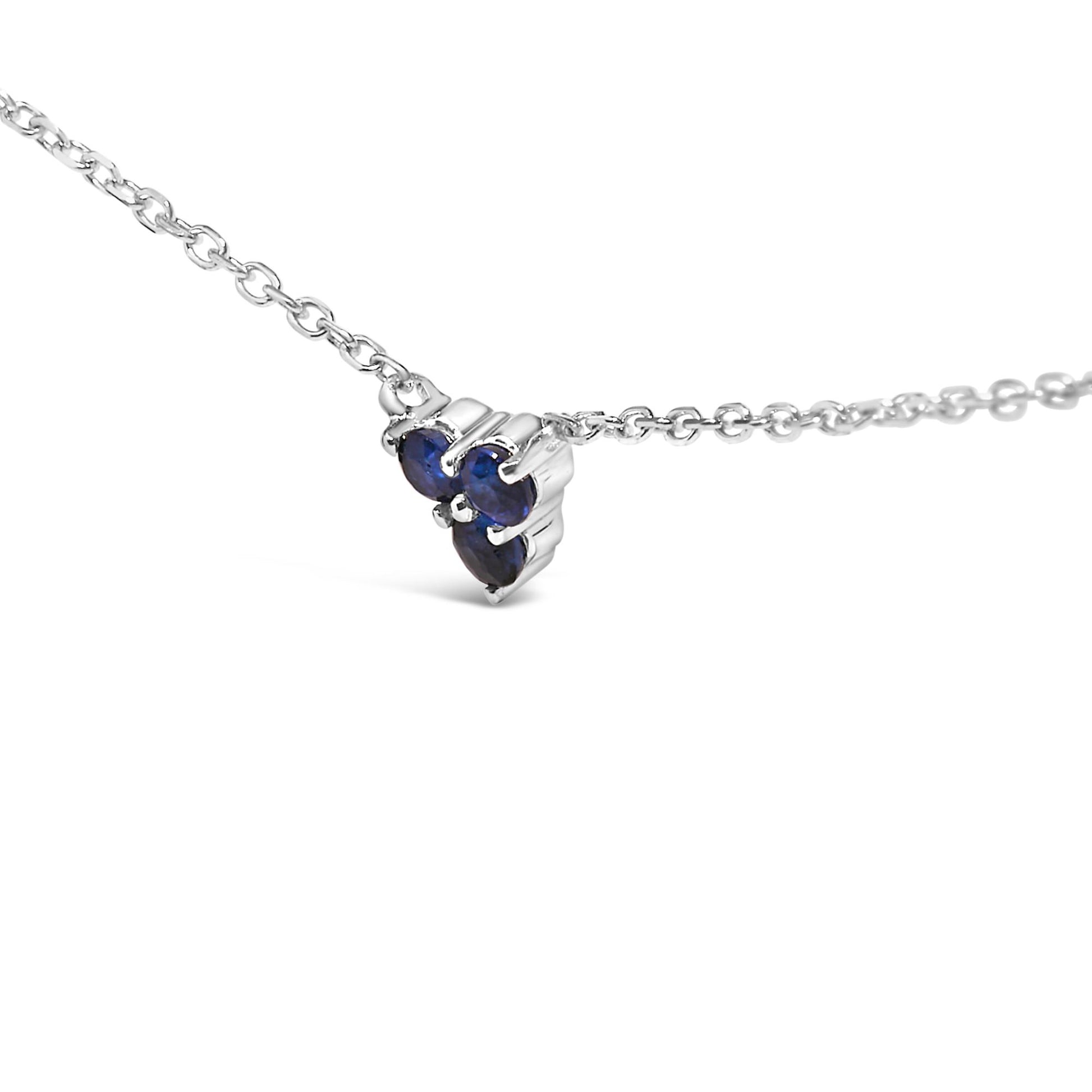 Close-up angled view of a white metal necklace with a small pendant featuring round blue gemstones in prong settings.