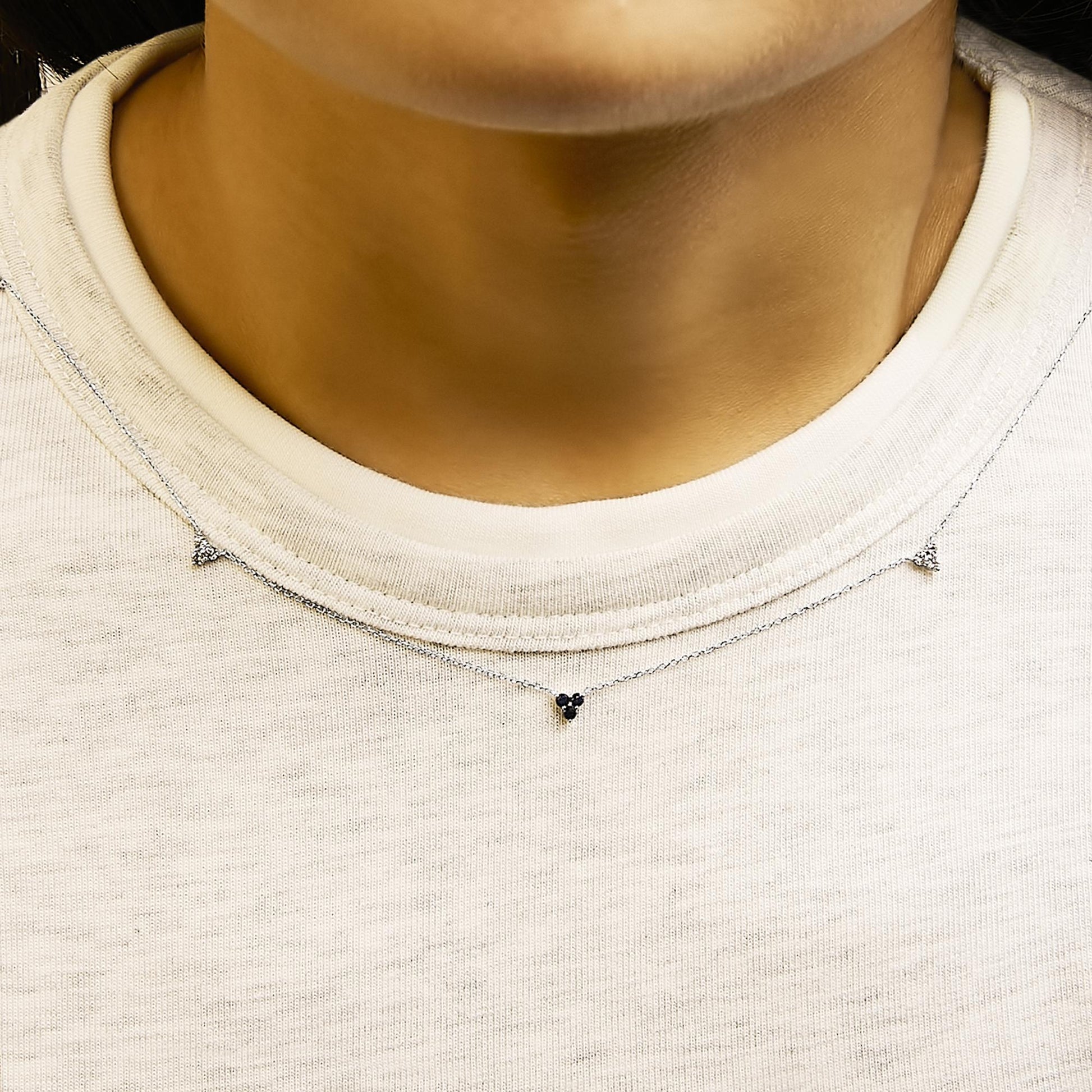 Close-up front view of a model wearing two delicate white metal necklaces, each with small clusters of round blue and white gemstones in prong settings.
