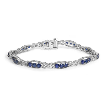 Close-up image of a white metal bracelet with alternating oval and twisted link design, featuring blue round gemstones and small white round gemstones in prong settings, shown flat from a slightly elevated front angle.
