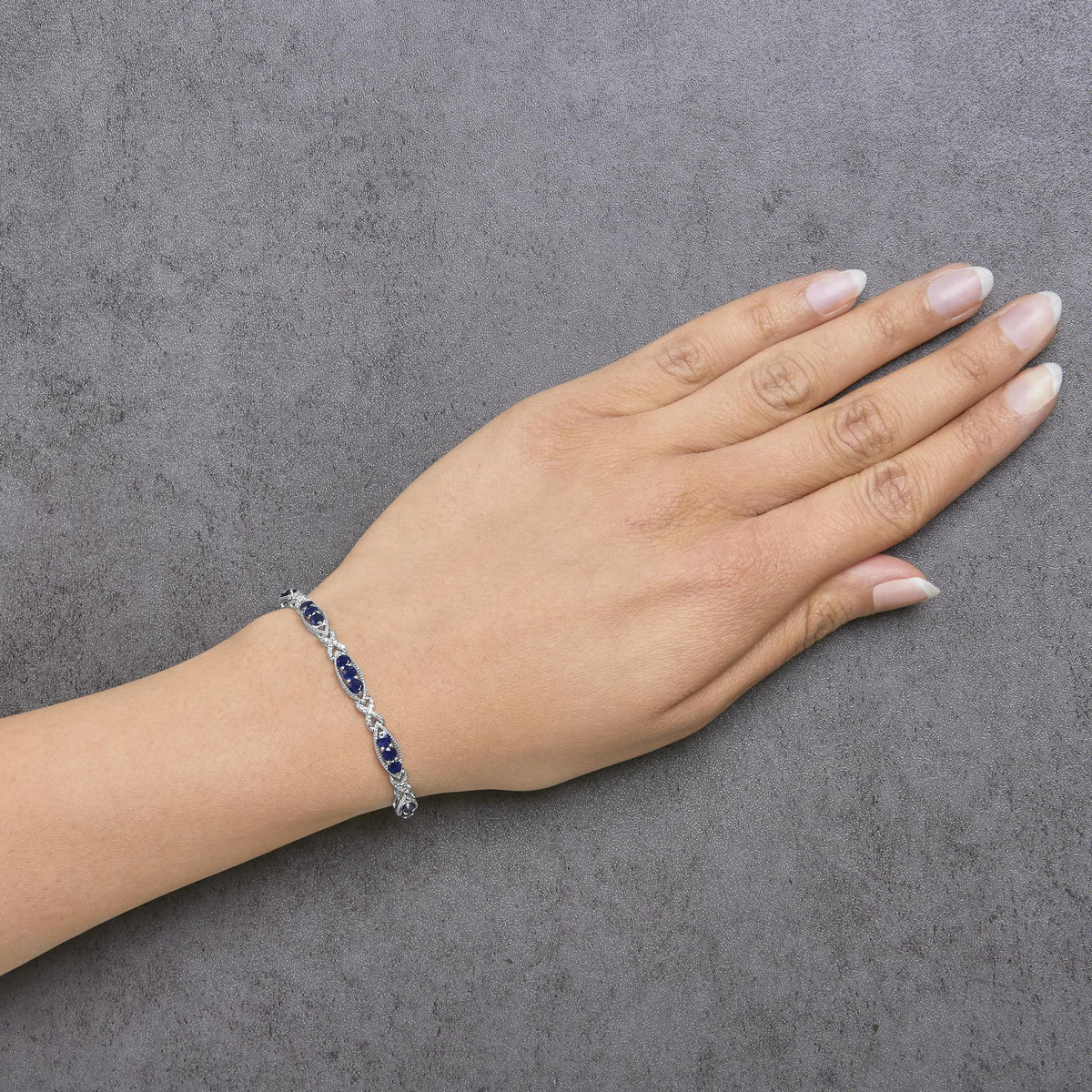White metal bracelet with alternating sections of round blue gemstones and white gemstones in prong settings, shown worn on a model's wrist, top-down angle.