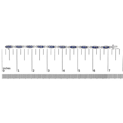 White bracelet with alternating oval sections containing blue gemstones and X-shaped links with white gemstones, shown on a scale, top-down view.